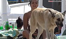 Amatőr lány kis mellekkel játszik egy kutyával a strandon